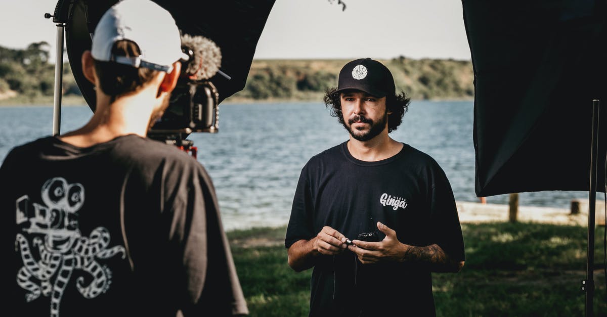 Do UK Immigration Officers record video when interviewing arrivers? - Male colleagues with video camera and walkie talkie standing on coast of pond while shooting film