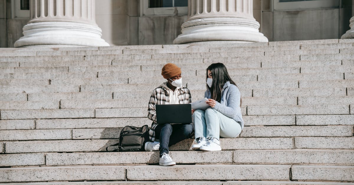 Do vouchers offered by EU airlines for Coronavirus cancellations turn into a full refund if not used? - Full body of young multiracial female friends in casual clothes with protective masks sitting on stairs near building and using laptop while talking in daytime
