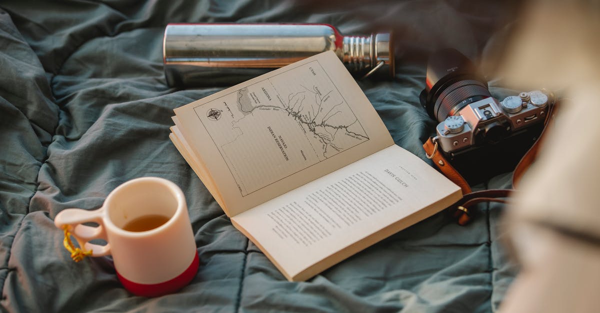Do you have to book motels in advance on a road-trip? - From above of open textbook between mug of hot drink and retro photo camera on crumpled fabric