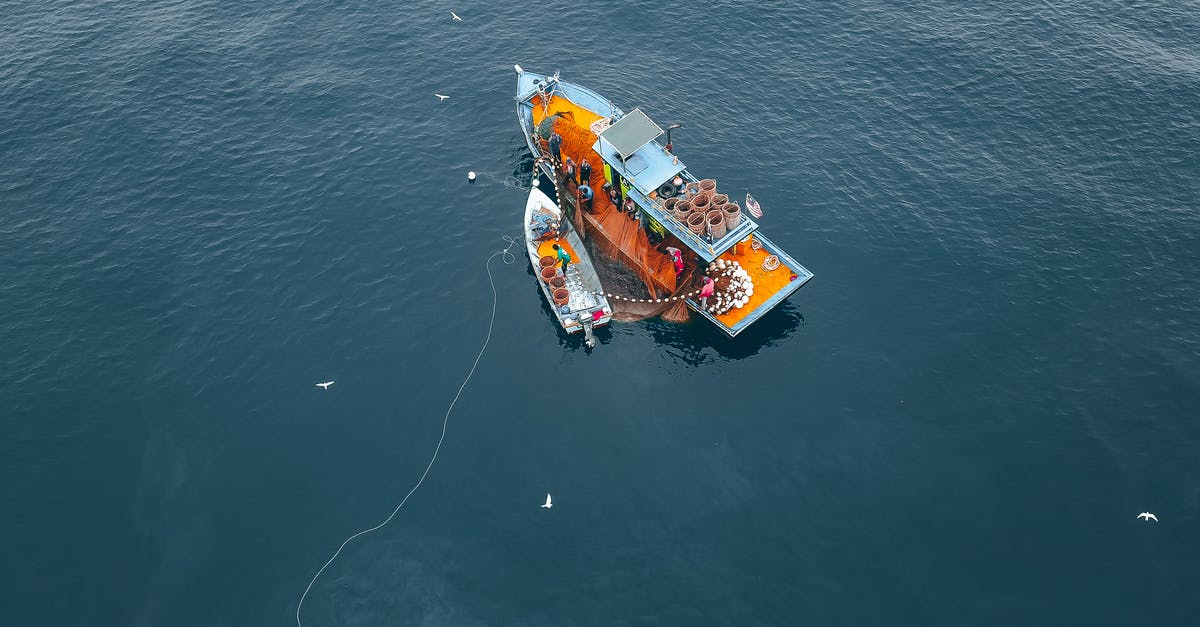 Do you need a visa to enter the US to catch another flight? [duplicate] - Drone view of boat and vessel moored on rippling sea water during traditional net fishing