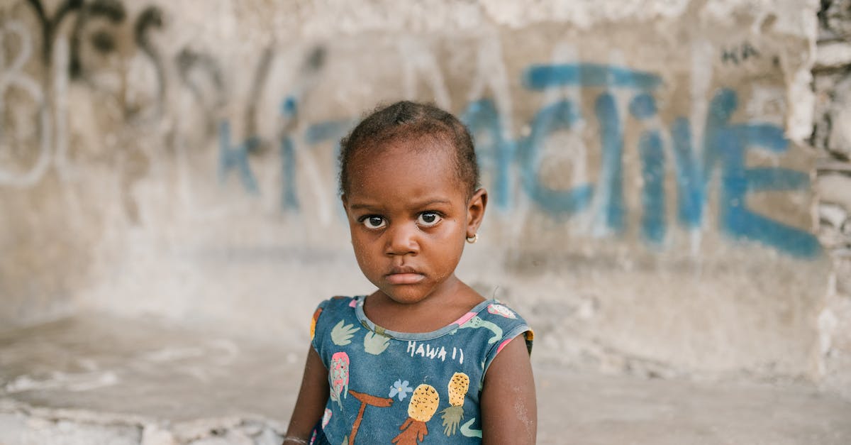 Do you need seperate visa for your children if they are registered in your passport - Frowning African American girl near weathered concrete building with vandal graffiti and broken wall in poor district