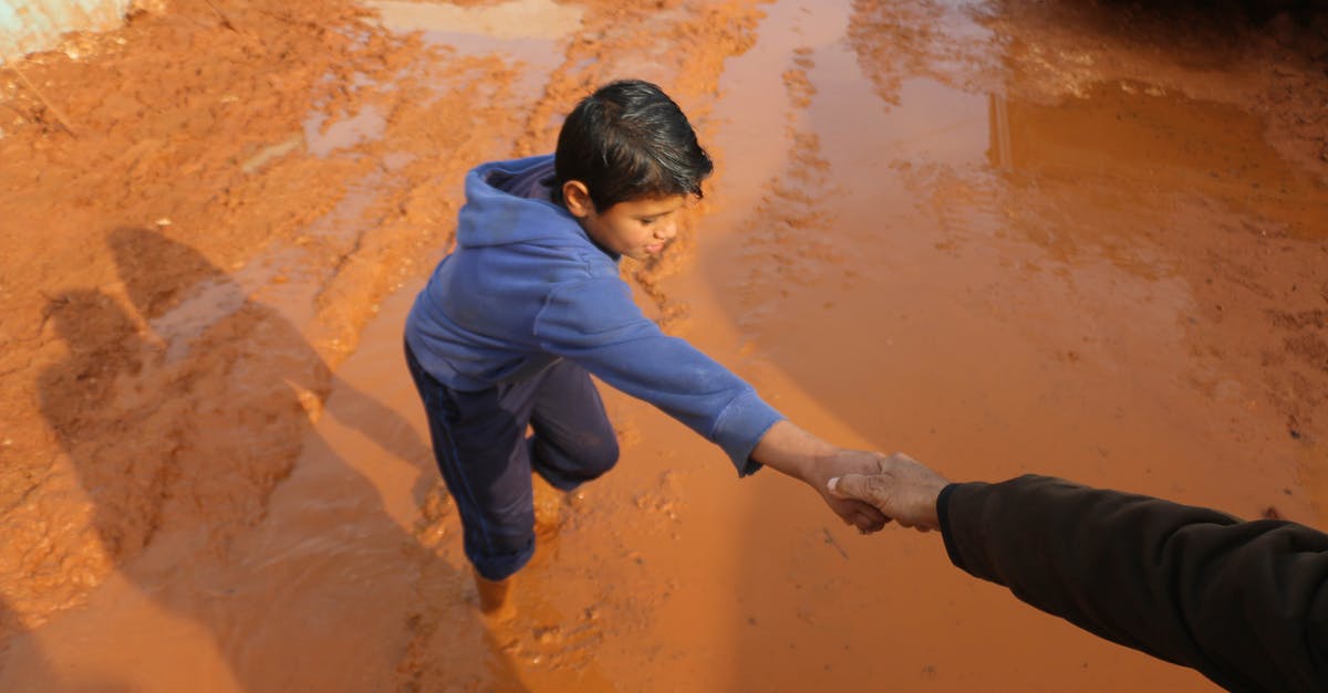 Does a Brazilian, who does not need a visa to visit the UK, need a visa if not arriving from Brazil? - High angle of crop person holding hands with ethnic boy stuck in dirty puddle in poor village