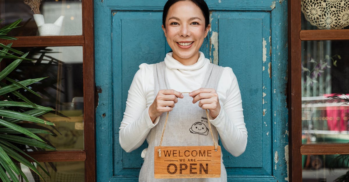 Does occupation show on a one visa affect your chances of getting visa for another country? - Cheerful ethnic female cafeteria owner in apron demonstrating cardboard signboard while standing near blue shabby door and windows after starting own business and looking at camera