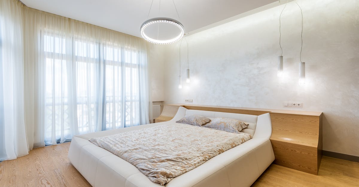 Double bed in Germany - Interior design of minimalistic modern bedroom furnished with comfortable bed and bedside nightstands decorated with ring shaped chandelier and lamps on ceiling Double bed in Germany - Interior design of minimalistic modern bedroom furnished with comfortable bed and bedside nightstands decorated with ring shaped chandelier and lamps on ceiling