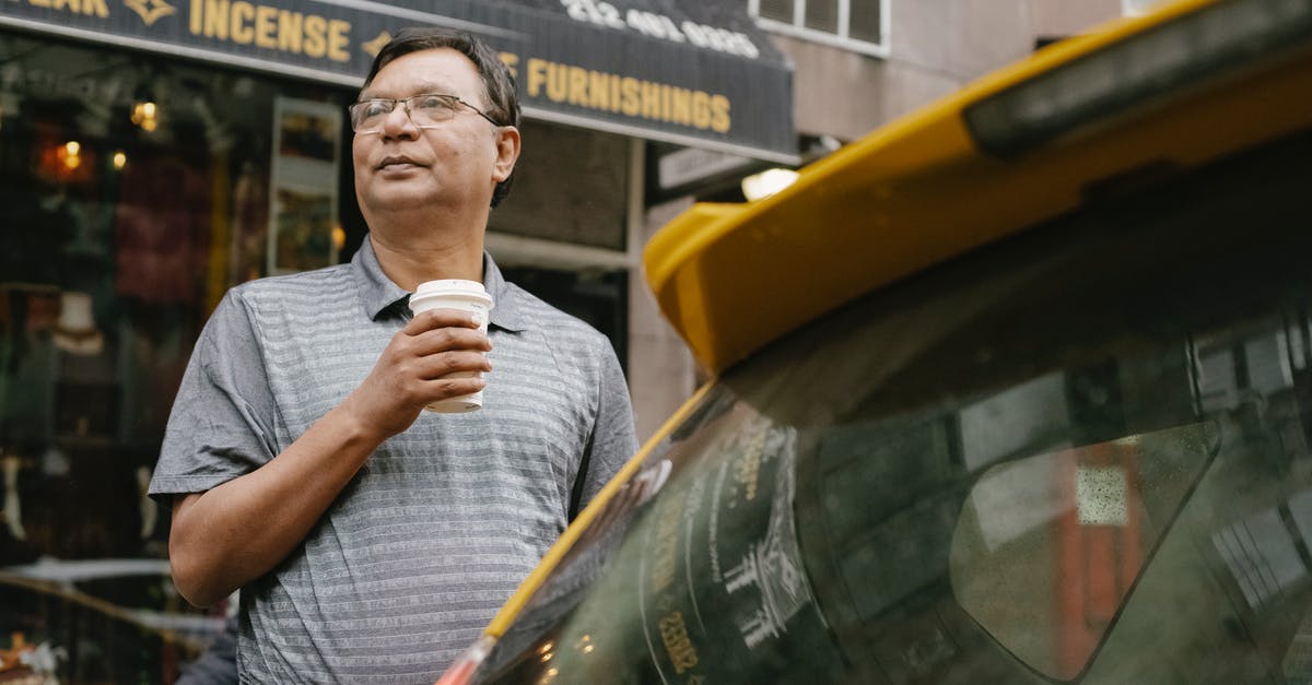 Drink driving ban in the UK applying for a Russian visa - Serious Asian middle aged male in eyeglasses looking away while standing with takeaway hot drink near yellow taxi and cafe on street Drink driving ban in the UK applying for a Russian visa - Serious Asian middle aged male in eyeglasses looking away while standing with takeaway hot drink near yellow taxi and cafe on street