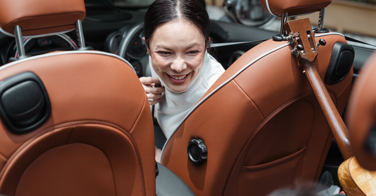 Driving from Genoa to The Hague with an LPG car - From above of smiling ethnic female driver turning back and looking at unrecognizable kid with ukulele during road trip Driving from Genoa to The Hague with an LPG car - From above of smiling ethnic female driver turning back and looking at unrecognizable kid with ukulele during road trip