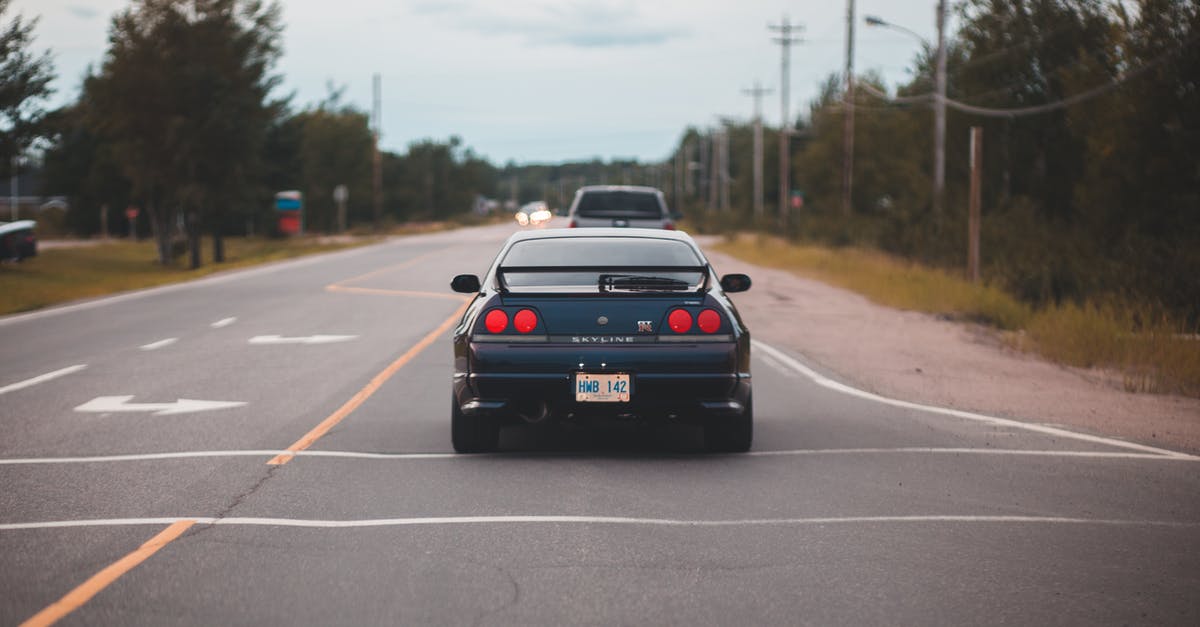 Driving in Chile with a Canadian N license - Rear bumper of luxury automobile on asphalt roadway with arrows between greenery trees under cloudy sky Driving in Chile with a Canadian N license - Rear bumper of luxury automobile on asphalt roadway with arrows between greenery trees under cloudy sky