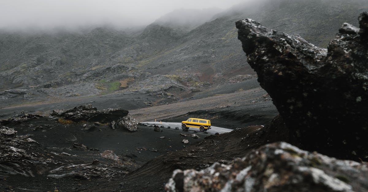 Driving in Iceland: a good idea? - Car driving on road between ridge under overcast sky Driving in Iceland: a good idea? - Car driving on road between ridge under overcast sky