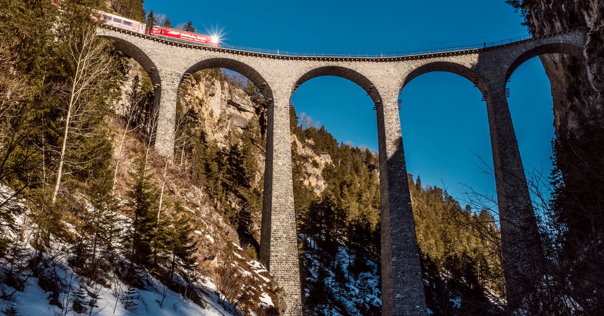 Driving in the winter (Dec-Jan) from Ohio to California - From below of train driving on arched bridge between mountains with coniferous trees under blue sky in wintertime Driving in the winter (Dec-Jan) from Ohio to California - From below of train driving on arched bridge between mountains with coniferous trees under blue sky in wintertime