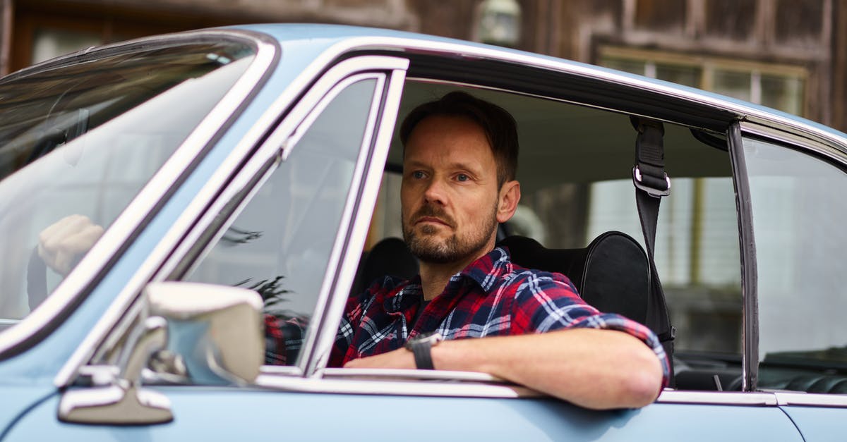Driving priority with a side road of different type surface - Adult thoughtful bearded driver in wristwatch and casual clothes driving blue automobile while passing by old building and looking away in daylight Driving priority with a side road of different type surface - Adult thoughtful bearded driver in wristwatch and casual clothes driving blue automobile while passing by old building and looking away in daylight