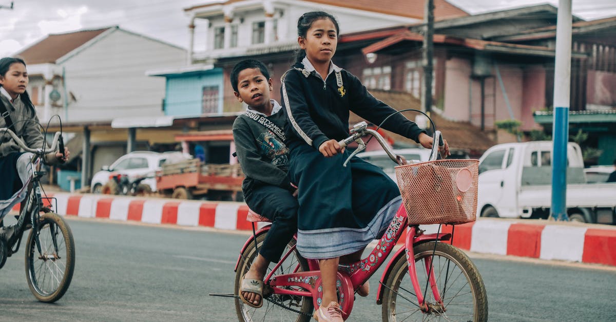 Driving priority with a side road of different type surface - Side view of ethnic siblings driving retro bicycle with basket on asphalt roadway in town Driving priority with a side road of different type surface - Side view of ethnic siblings driving retro bicycle with basket on asphalt roadway in town