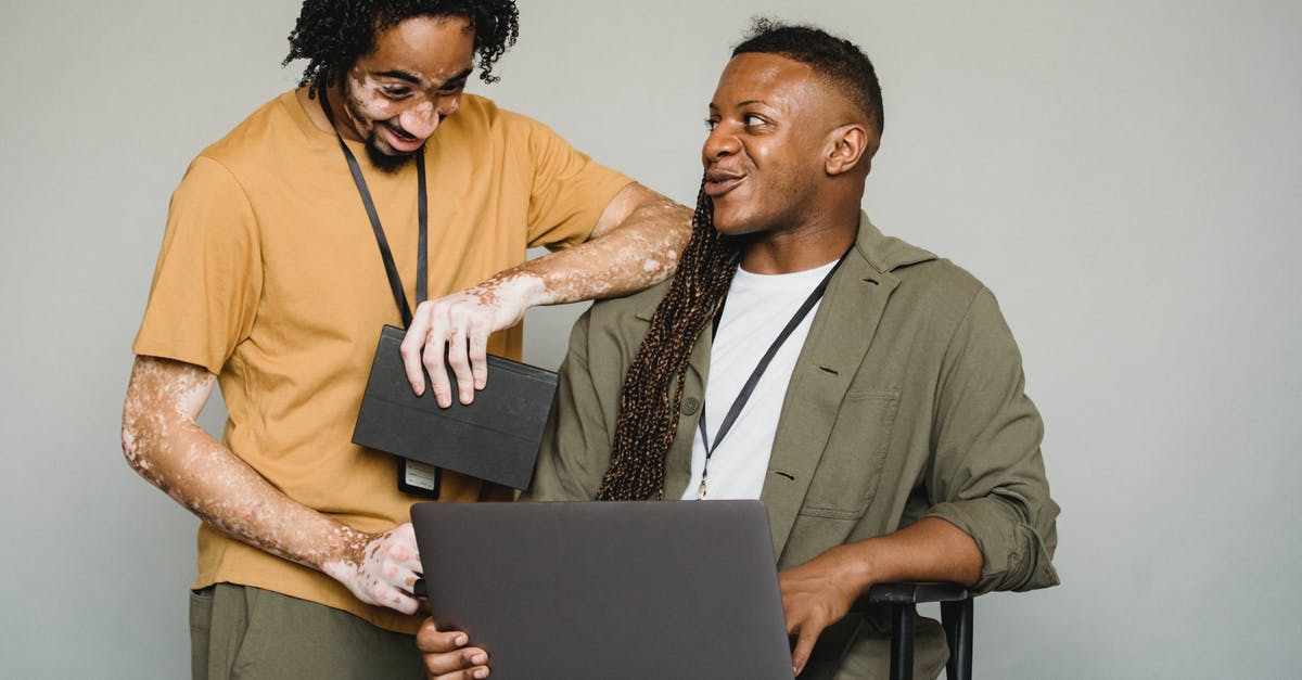 Dual Passports with two different last names. - Happy African American androgynous person with Afro braids and computer looking at black colleague with vitiligo and notebook while working on gray background
