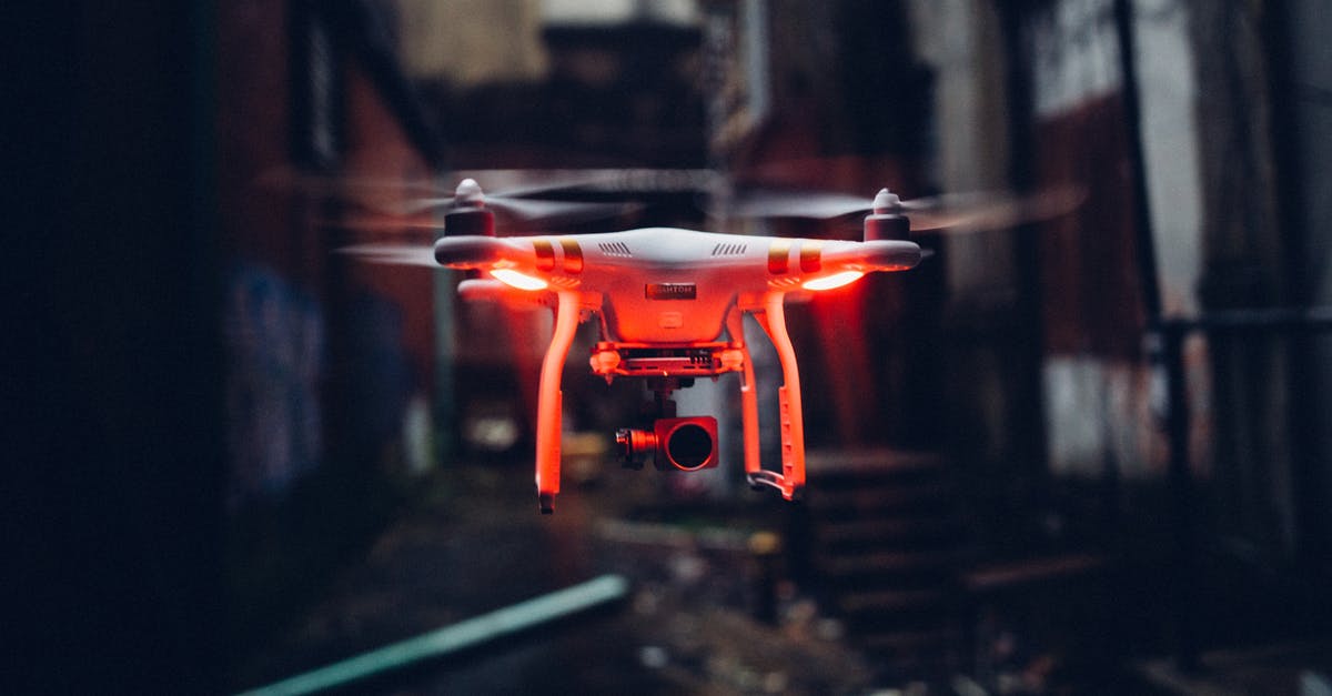 Electronic devices security on airplanes - Red glowing modern drone flying in air on blurred background of gloomy industrial street Electronic devices security on airplanes - Red glowing modern drone flying in air on blurred background of gloomy industrial street