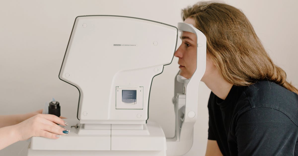 Electronic medical devices through British airport security - Side view of crop anonymous doctor checking eyesight of female patient using vision screening device in clinic Electronic medical devices through British airport security - Side view of crop anonymous doctor checking eyesight of female patient using vision screening device in clinic