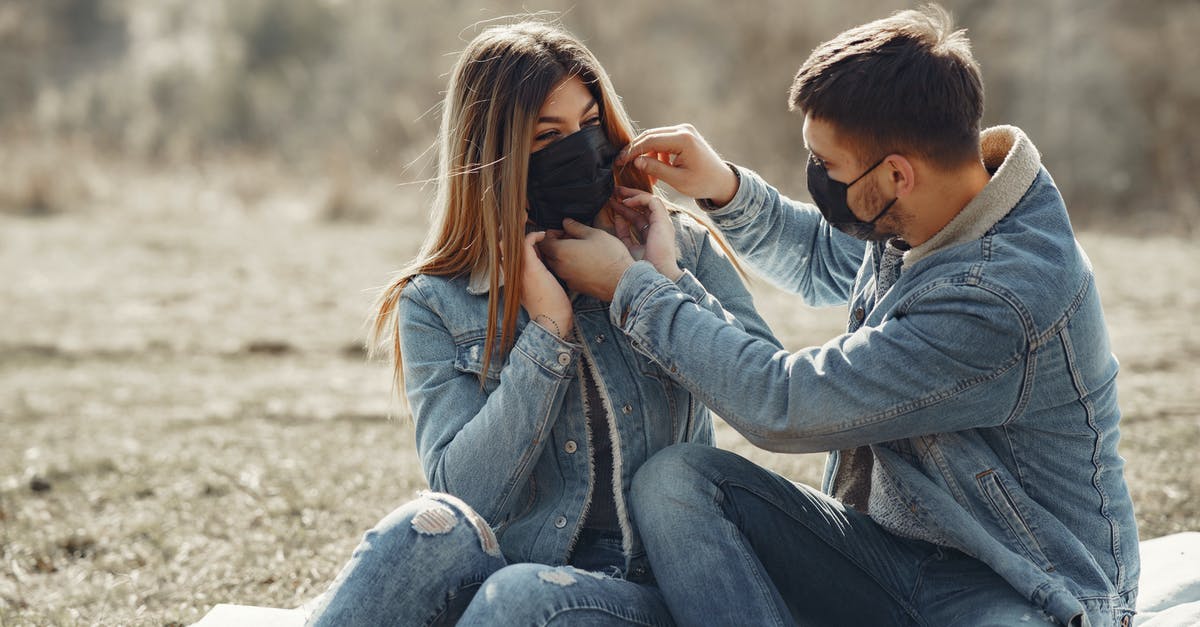 ESTA 90 day start date - Cheerful young couple in black medical masks resting on plaid on sunny meadow in countryside ESTA 90 day start date - Cheerful young couple in black medical masks resting on plaid on sunny meadow in countryside