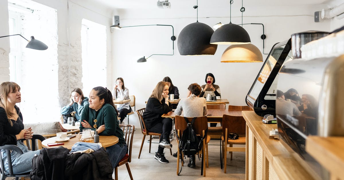 ESTA visiting the US twice for 40 days each with a 20 day break in between - Group of multiracial friends in casual wear sitting at wooden tables in cozy cafeteria near cash box and big lamps while conversing