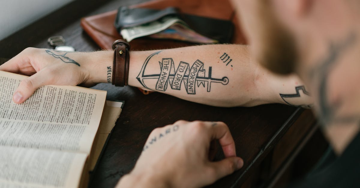 E-Ticket vs Itinerary vs Booking Reference - Crop man with tattoo on arm reading old book E-Ticket vs Itinerary vs Booking Reference - Crop man with tattoo on arm reading old book