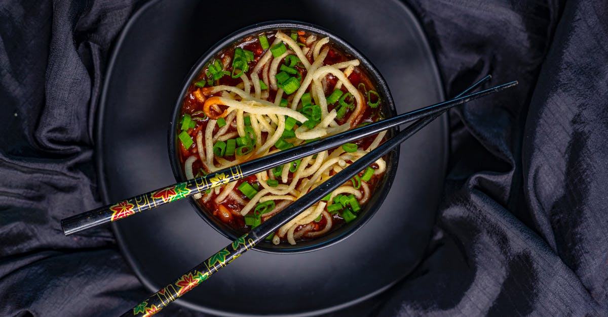 Etiquette of eating noodle soup in China - Top view of black bowl with Asian soup with noodle and green onion served with bamboo chopsticks on black tablecloth Etiquette of eating noodle soup in China - Top view of black bowl with Asian soup with noodle and green onion served with bamboo chopsticks on black tablecloth