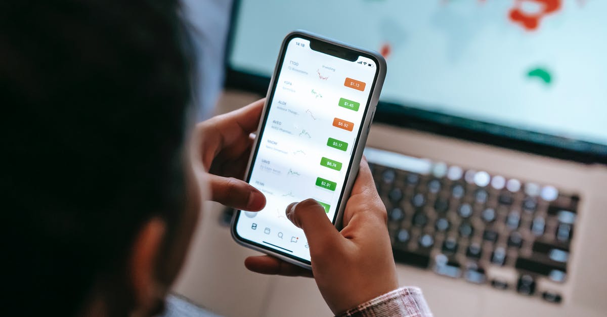 Exchanging and using Scottish pounds - Crop broker using trading app on smartphone against laptop Exchanging and using Scottish pounds - Crop broker using trading app on smartphone against laptop
