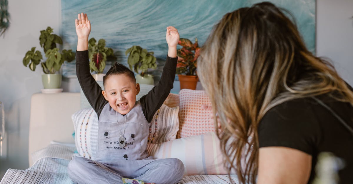 Expenditure in Poland - Forex Card doesn't have Złoty - Happy boy raising arms after winning card game sitting on bed with unrecognizable mother Expenditure in Poland - Forex Card doesn't have Złoty - Happy boy raising arms after winning card game sitting on bed with unrecognizable mother