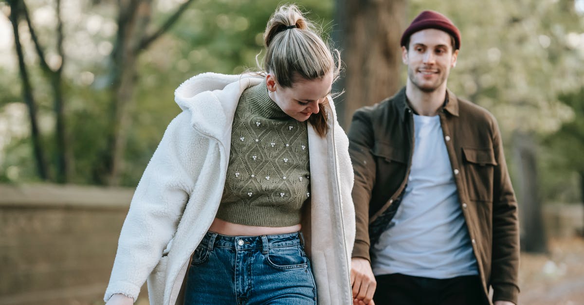 Expiration of a Delta ecredit following a changed date - Cheerful young stylish lady in warm clothes holding hand of smiling boyfriend while walking together in park on sunny autumn day