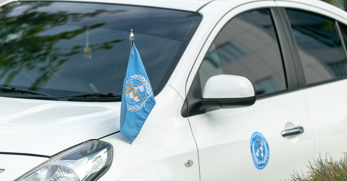 Exploring Switzerland with a car - where can I park? - Contemporary white car decorated with blue World Health Organization flag and sticker parked on street Exploring Switzerland with a car - where can I park? - Contemporary white car decorated with blue World Health Organization flag and sticker parked on street