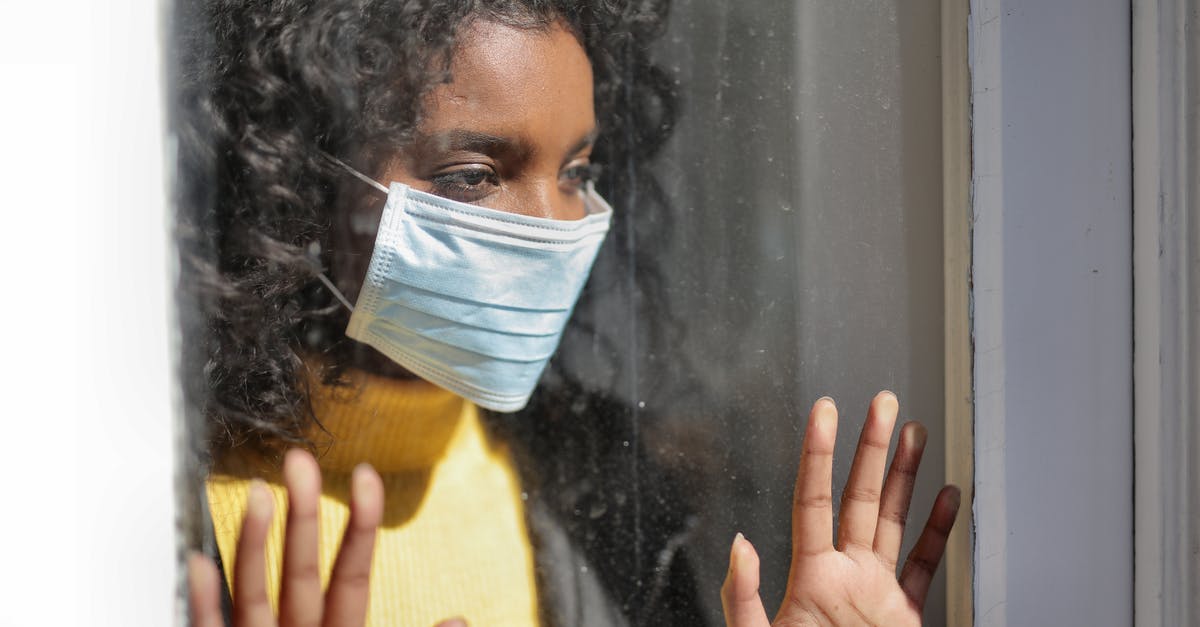 Extension of stay at USA due to COVID-19 lockdown - Serious young ethnic lady in medical mask standing near window and looking away on street Extension of stay at USA due to COVID-19 lockdown - Serious young ethnic lady in medical mask standing near window and looking away on street