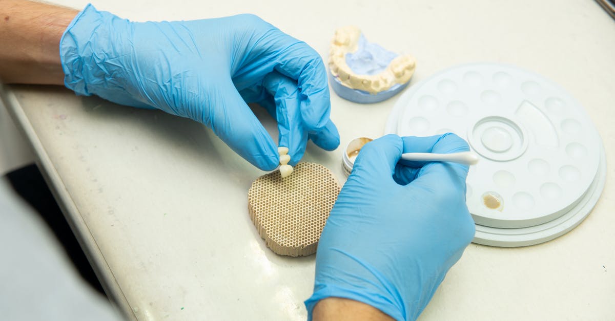 Fake work permit and deportation - From above of crop anonymous orthodontist in latex gloves creating fake teeth for denture while sitting at table in light dental clinic Fake work permit and deportation - From above of crop anonymous orthodontist in latex gloves creating fake teeth for denture while sitting at table in light dental clinic