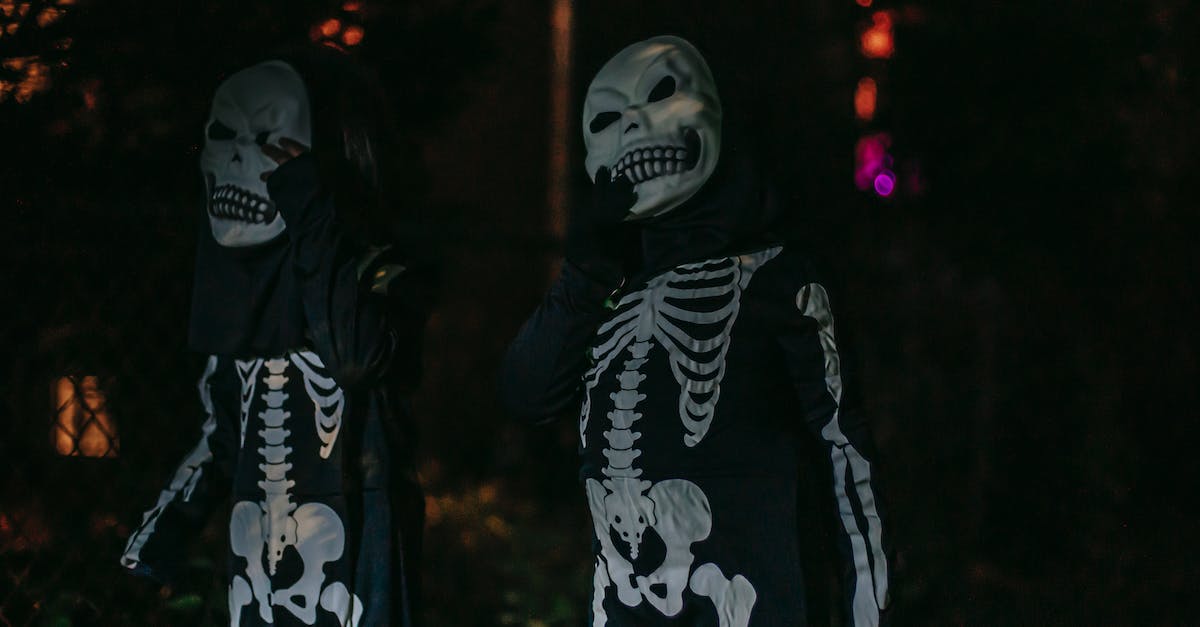 Fall events in Madrid - Unrecognizable persons dressed in costumes of skeleton standing on dark street Fall events in Madrid - Unrecognizable persons dressed in costumes of skeleton standing on dark street