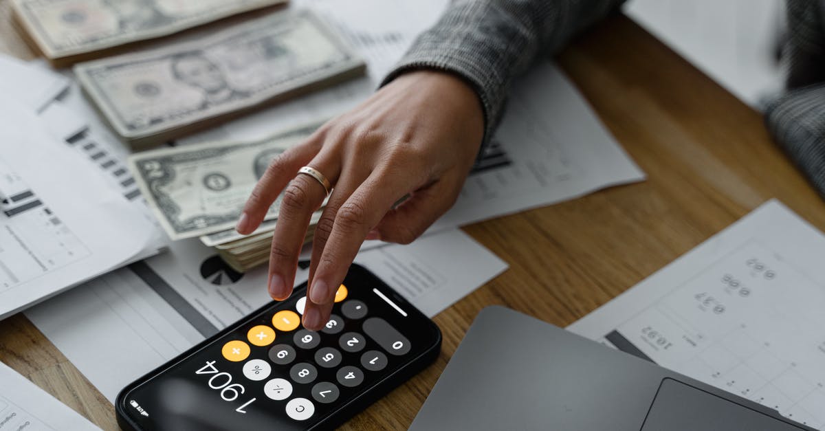 Fee for taking cash out of the EU - Hand of a Person Using a Calculator Near Cash Money on Wooden Table Fee for taking cash out of the EU - Hand of a Person Using a Calculator Near Cash Money on Wooden Table