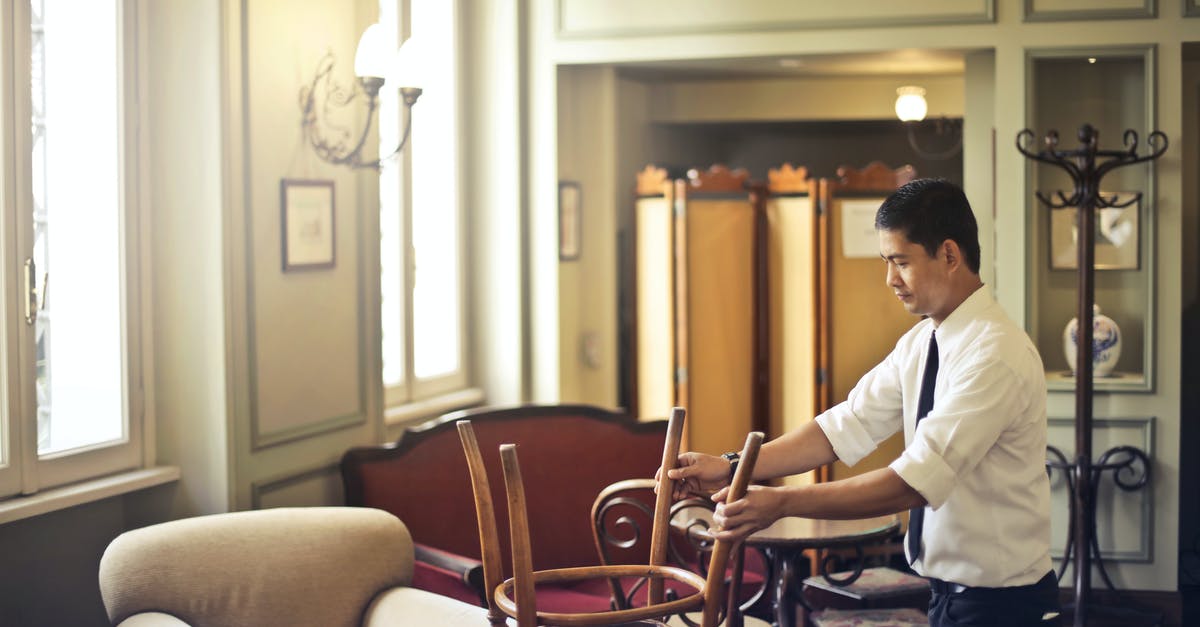 Finding Restaurants - Restaurant Guides, Consumer Reviews, Professional Critics’ Reviews? [closed] - Side view of Asian male employee in formal wear standing near table and neatly stacking wooden chair on table in closed restaurant