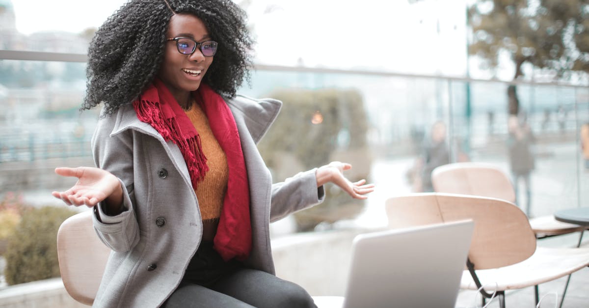 Finding sleepover spots in internet cafes in Japan? - Happy excited African American female laughing and gesticulating while having video calling on laptop and sitting at modern cafe