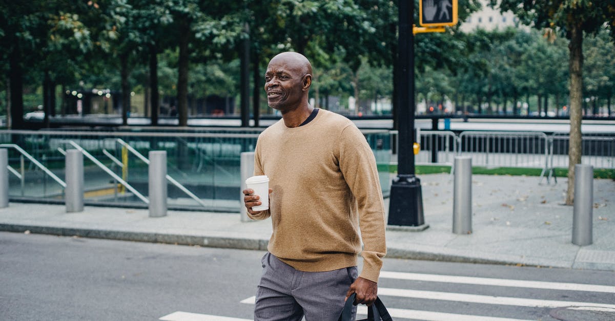 Flying from Geneva to Frankfurt to San Francisco, will my carry on bag go through the x-ray again at Frankfurt airport? - Mature African American man carrying disposable coffee cup and personal bag crossing street in downtown