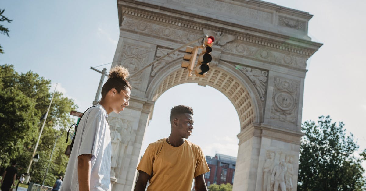 Flying stand by from US to Europe -- is it still worth it, and if so, how to do it? - From below of multiethnic male skateboarders standing against aged stone Triumphal Arch in USA