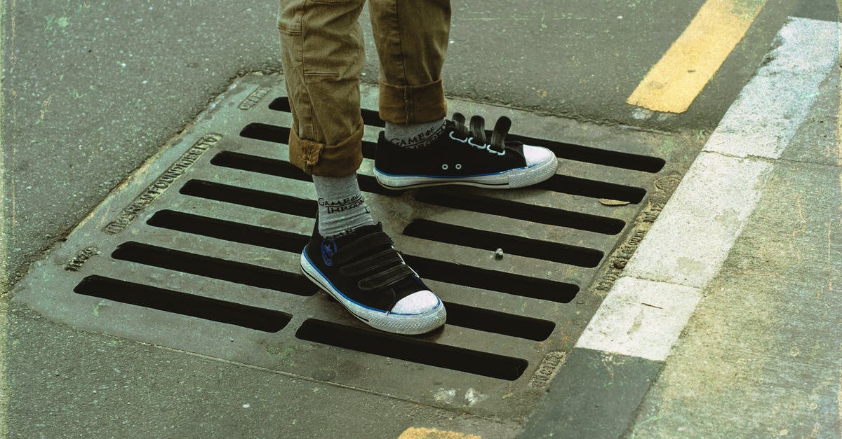 Flying stand by from US to Europe -- is it still worth it, and if so, how to do it? - From above crop anonymous male legs in casual wear standing on asphalt road sewerage steel grating in daylight