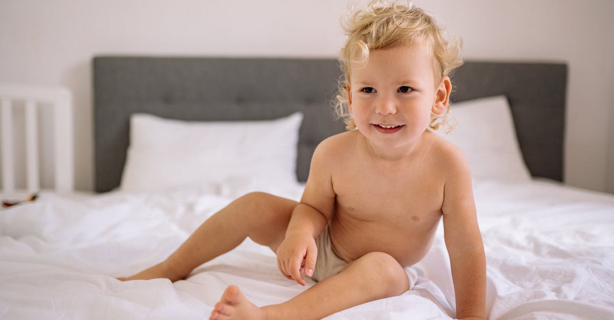 Flying with a baby, changing diapers onboard - Happy Toddler Sitting on Bed Flying with a baby, changing diapers onboard - Happy Toddler Sitting on Bed