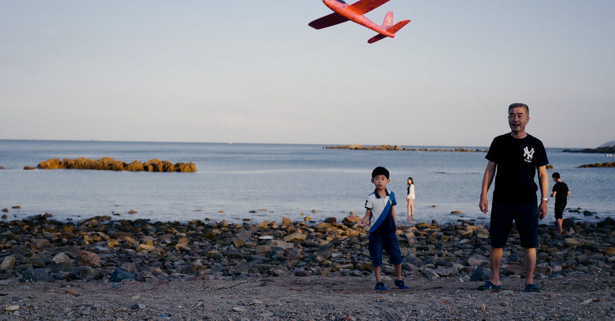 Flying with a lap child on a code shared flight - Ethnic father and son launching toy plane on beach at sunset Flying with a lap child on a code shared flight - Ethnic father and son launching toy plane on beach at sunset