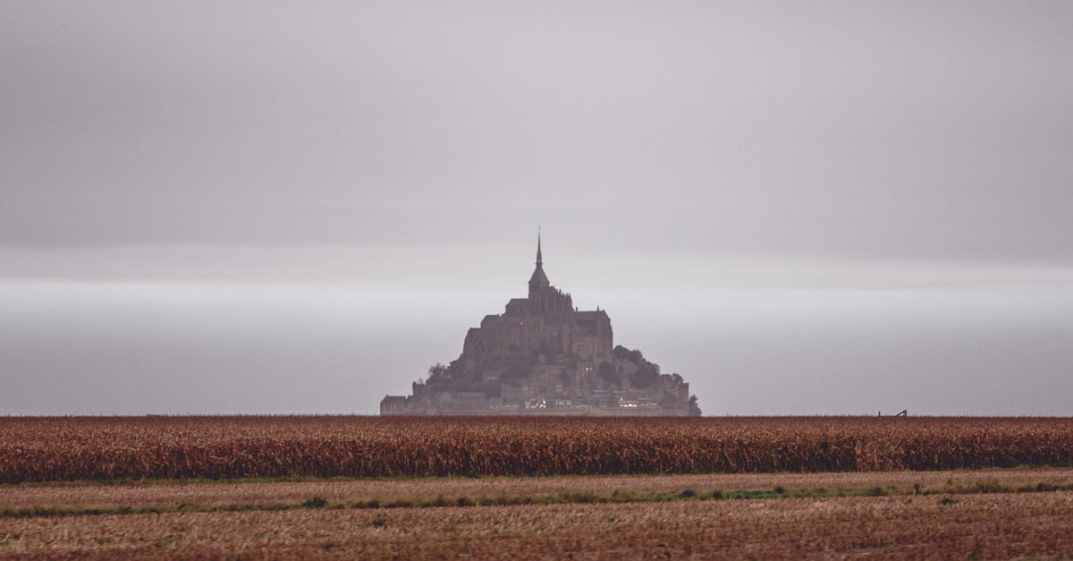 France visa processing time in Dubai per nationality - Scenery of distant grand Mon Saint Michel Abbey situated on vast grassy valley under cloudy gloomy sky France visa processing time in Dubai per nationality - Scenery of distant grand Mon Saint Michel Abbey situated on vast grassy valley under cloudy gloomy sky