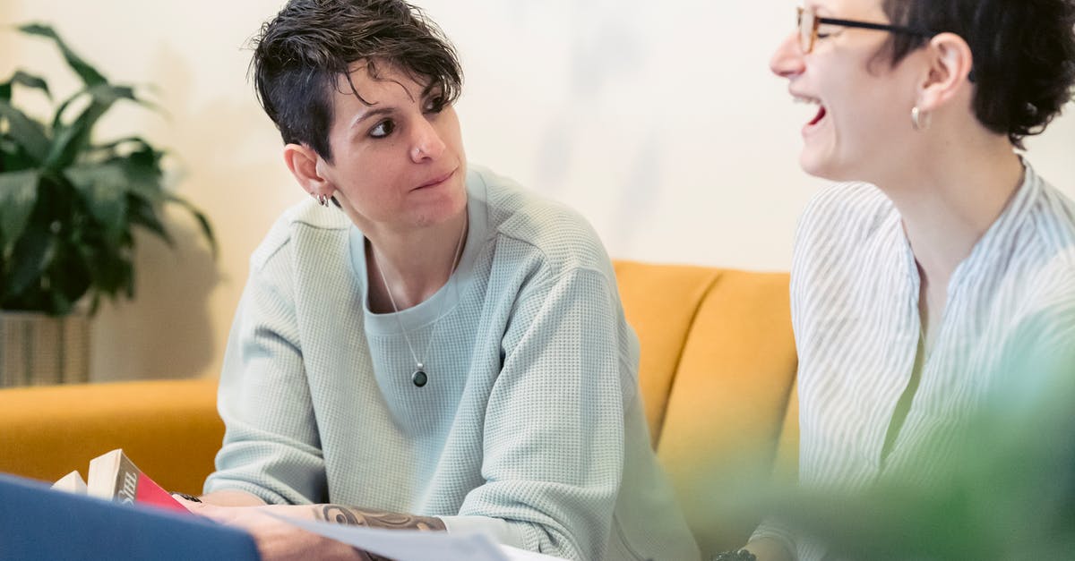Friend wants to work in UK and is qualified but can she do so legally? [closed] - Crop cheerful young woman with short dark hair laughing with closed eyes while working remotely on laptop at home sitting on sofa with female friend