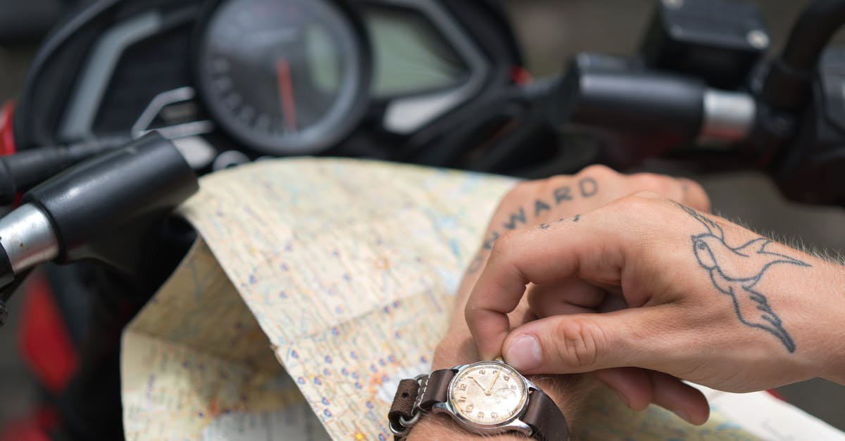 From JFK to Newark. Time & transportation alternatives - Crop tattooed man setting up watch against map and motorbike From JFK to Newark. Time & transportation alternatives - Crop tattooed man setting up watch against map and motorbike