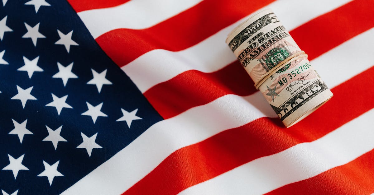 Funding friend's visit to UK from USA - From above of United States currency folded in roll placed on USA flag illustrating concept of business profit and wealth Funding friend's visit to UK from USA - From above of United States currency folded in roll placed on USA flag illustrating concept of business profit and wealth
