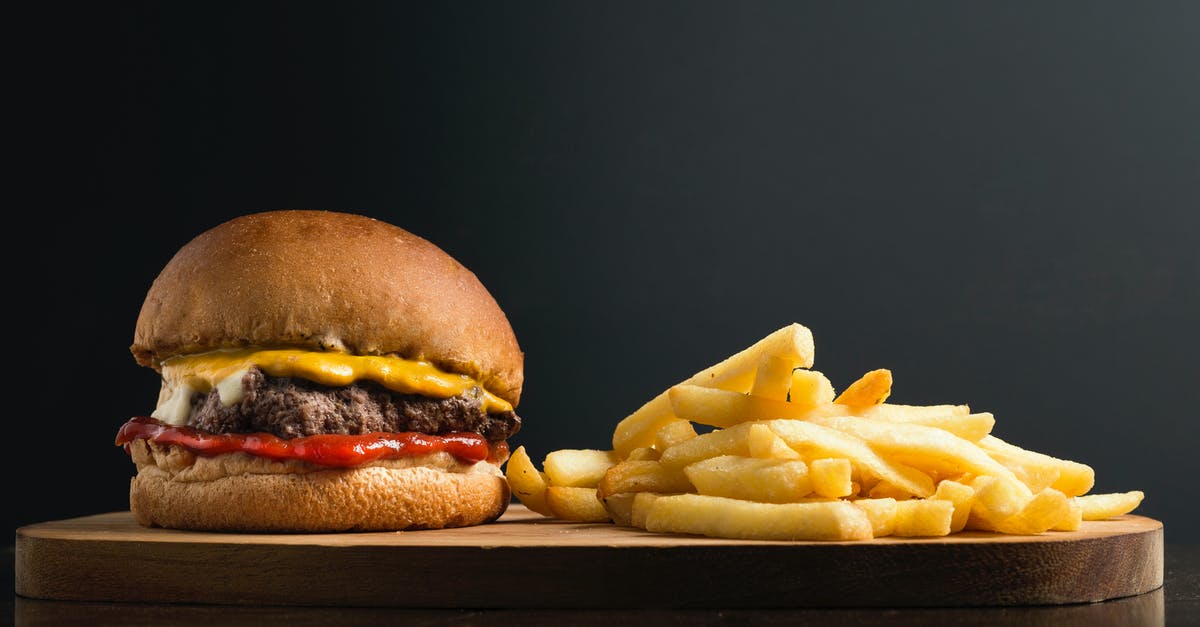 Geneva to Chamonix with French Issued Visa - Appetizing burger with meat patty ketchup and cheese placed on wooden table with crispy french fries against black background Geneva to Chamonix with French Issued Visa - Appetizing burger with meat patty ketchup and cheese placed on wooden table with crispy french fries against black background
