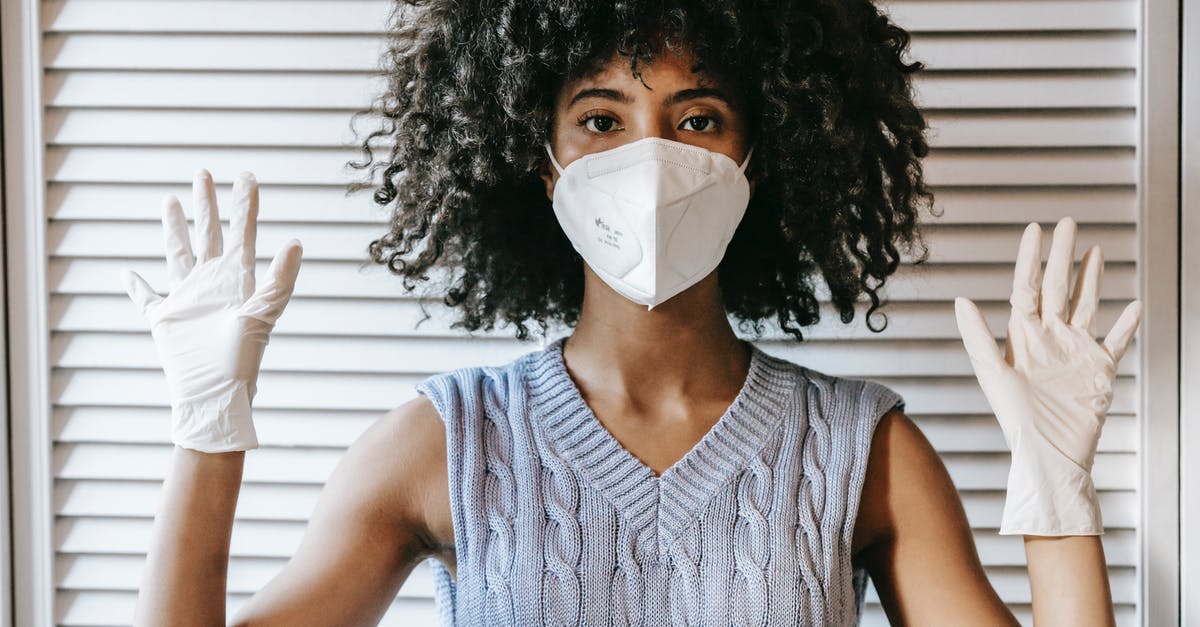 Germany Layover Covid Restrictions - Young African American female wearing white protective face mask and medical white rubber gloves with hands raised looking at camera Germany Layover Covid Restrictions - Young African American female wearing white protective face mask and medical white rubber gloves with hands raised looking at camera