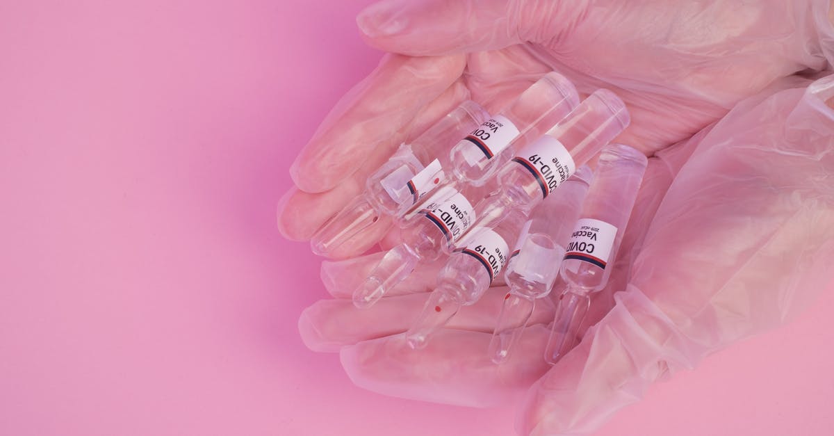 Get 2nd dose of COVID vaccine in the US as a tourist - Top view of crop faceless female doctor in latex gloves demonstrating heap of ampoules with COVID vaccine against pink background Get 2nd dose of COVID vaccine in the US as a tourist - Top view of crop faceless female doctor in latex gloves demonstrating heap of ampoules with COVID vaccine against pink background