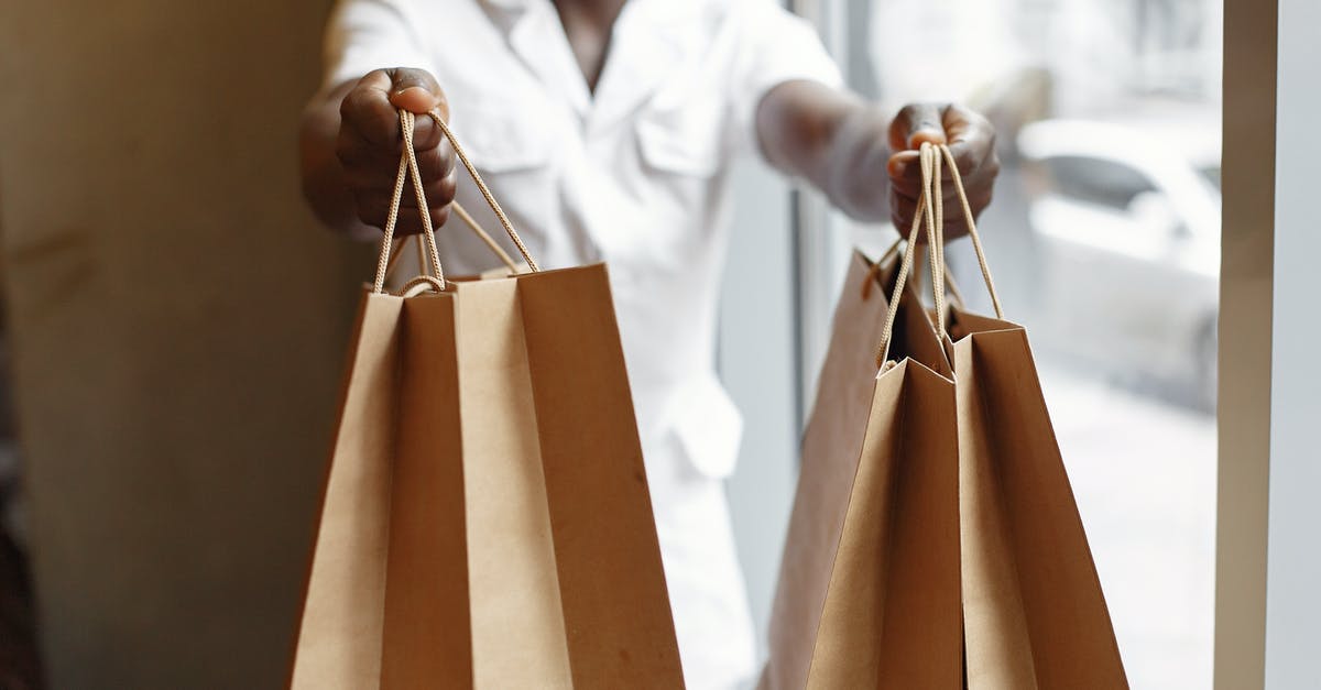 Give Delta voucher to another person - Crop anonymous African American person in white jacket passing purchases in paper shopping bags while standing near window in daylight Give Delta voucher to another person - Crop anonymous African American person in white jacket passing purchases in paper shopping bags while standing near window in daylight