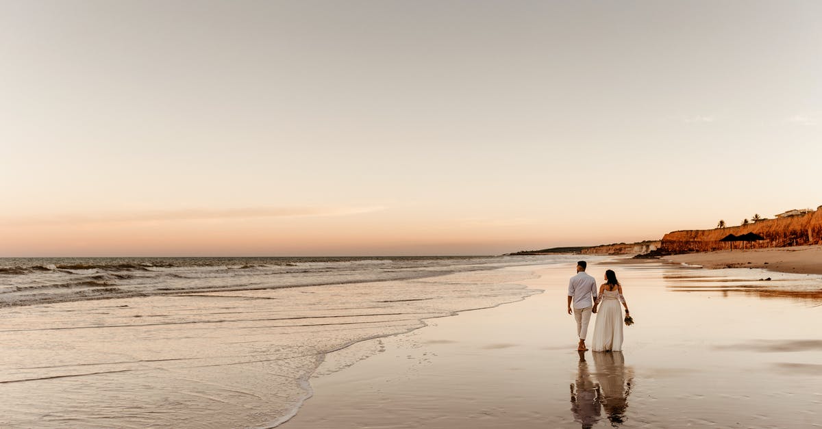 Going back to the USA on ESTA after K1 visa and marriage - Back view of barefoot groom holding hand of bride in white dress and walking together on sandy coast