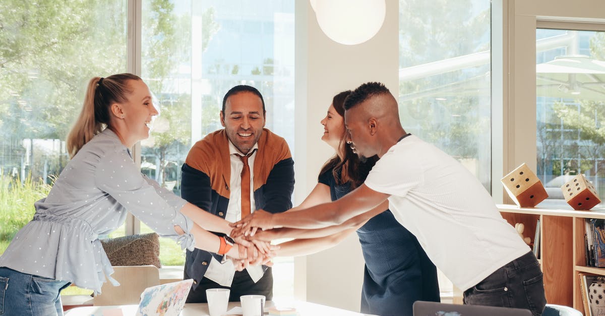 Group visa applied but not received for one member - Content multiethnic colleagues joining hands above table with laptops in modern office on sunny day Group visa applied but not received for one member - Content multiethnic colleagues joining hands above table with laptops in modern office on sunny day