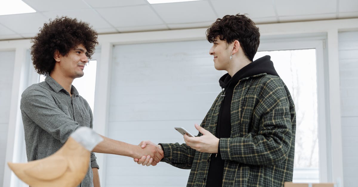 Handshake while holding own right elbow - A Man Holding a Smartphone Shaking Hands with a Man in Gray Shirt Handshake while holding own right elbow - A Man Holding a Smartphone Shaking Hands with a Man in Gray Shirt