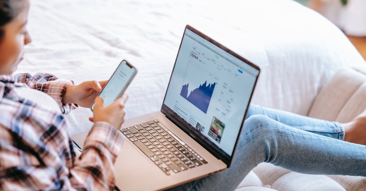 Home exchange sites? - Crop ethnic trader using smartphone against laptop at home Home exchange sites? - Crop ethnic trader using smartphone against laptop at home