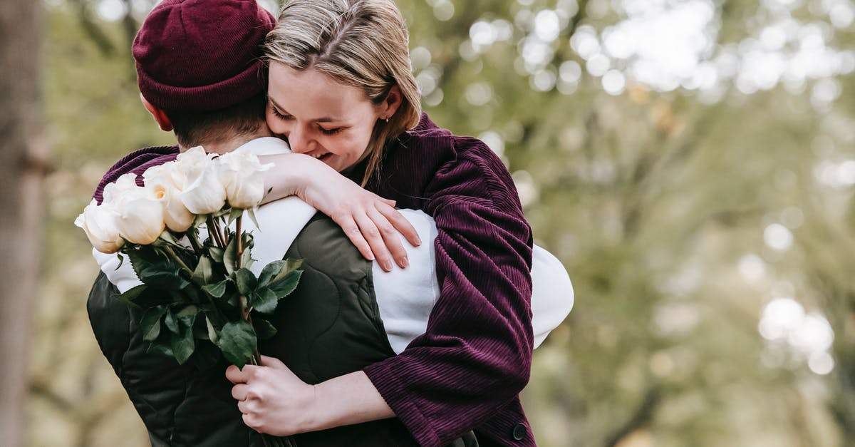 Honeymoon package times? - Young cheerful girlfriend with gentle white roses embracing anonymous boyfriend on blurred background of trees Honeymoon package times? - Young cheerful girlfriend with gentle white roses embracing anonymous boyfriend on blurred background of trees
